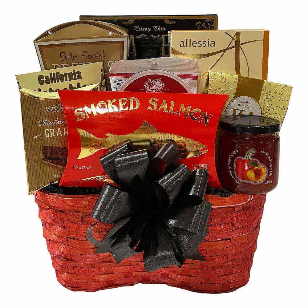 Red wicker gift basket filled with assorted gourmet treats including smoked salmon, chocolate graham crackers, English breakfast tea, and spreads with a black decorative bow.